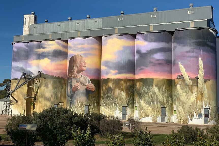 Colourful painted silos showing a young girl standing in a field of wheat.