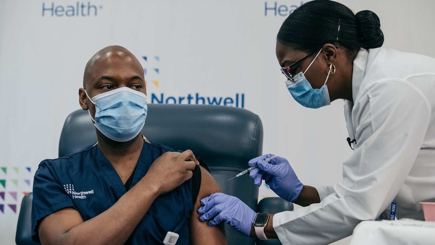 An African American woman injecting a vaccine in the upper arm of an African American man