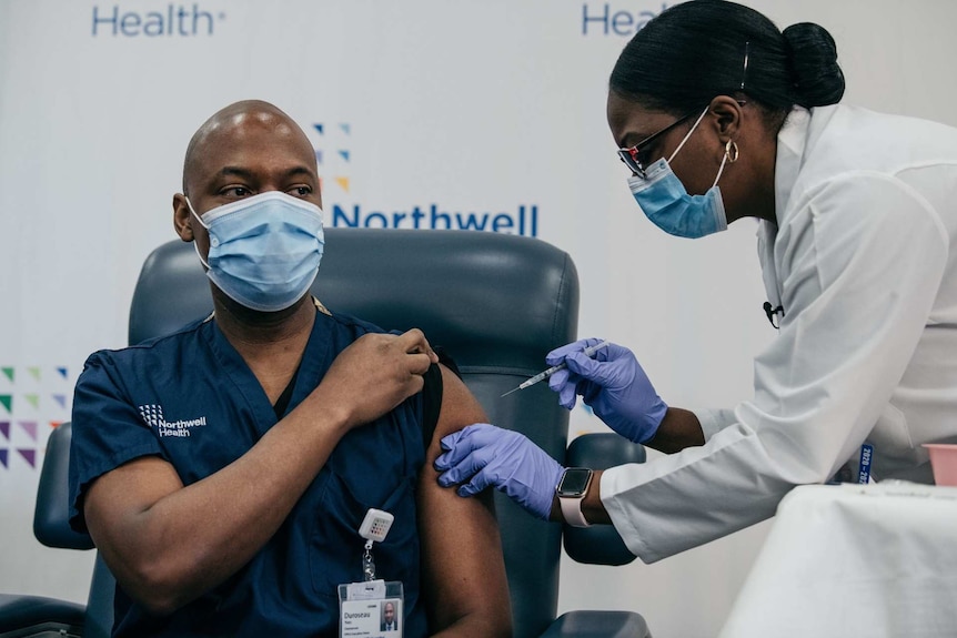 An African American woman injecting a vaccine in the upper arm of an African American man