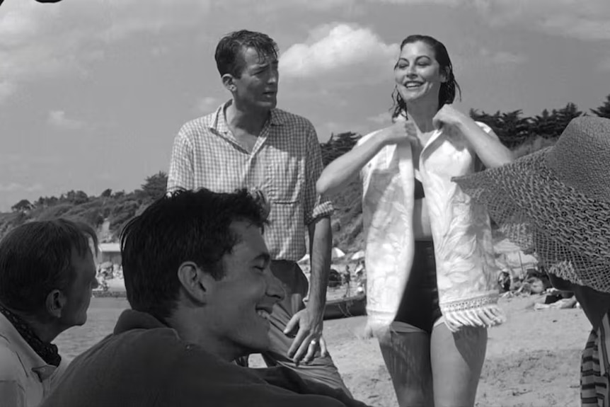 A black and white photo of a man in a check shirt and a woman in a white top on a beach behind a group of people