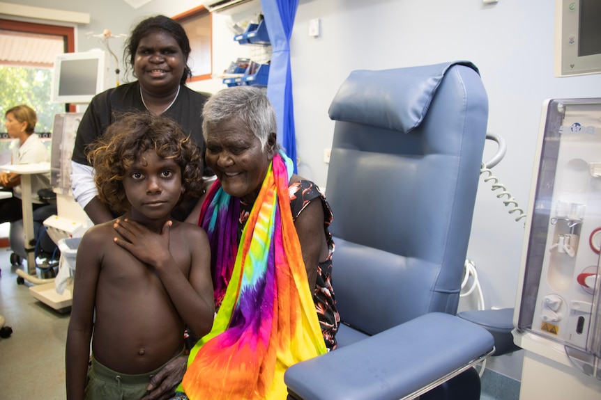 A woman sits on a dialysis chair with her family.