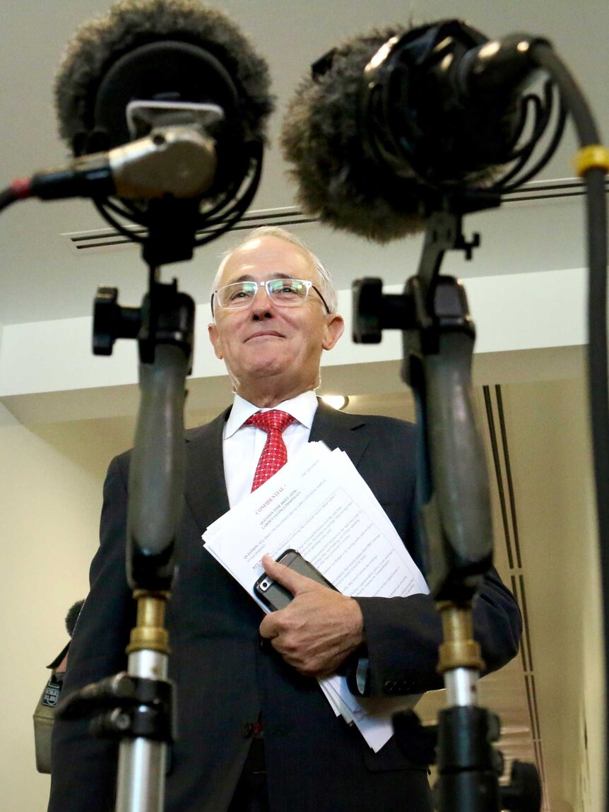 Down low angle through two microphones of Malcolm Turnbull approaching the assembled media.