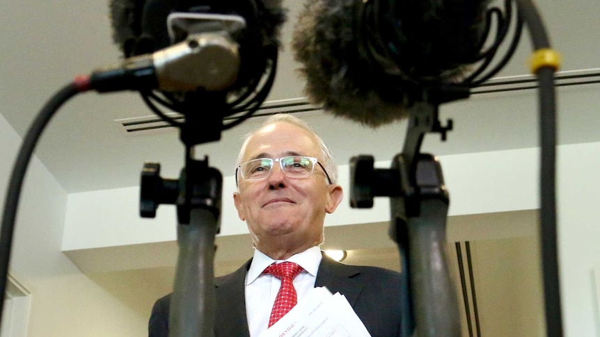 Down low angle through two microphones of Malcolm Turnbull approaching the assembled media.