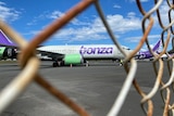 A Bonza plane sits on the tarmac behind a wire fence.