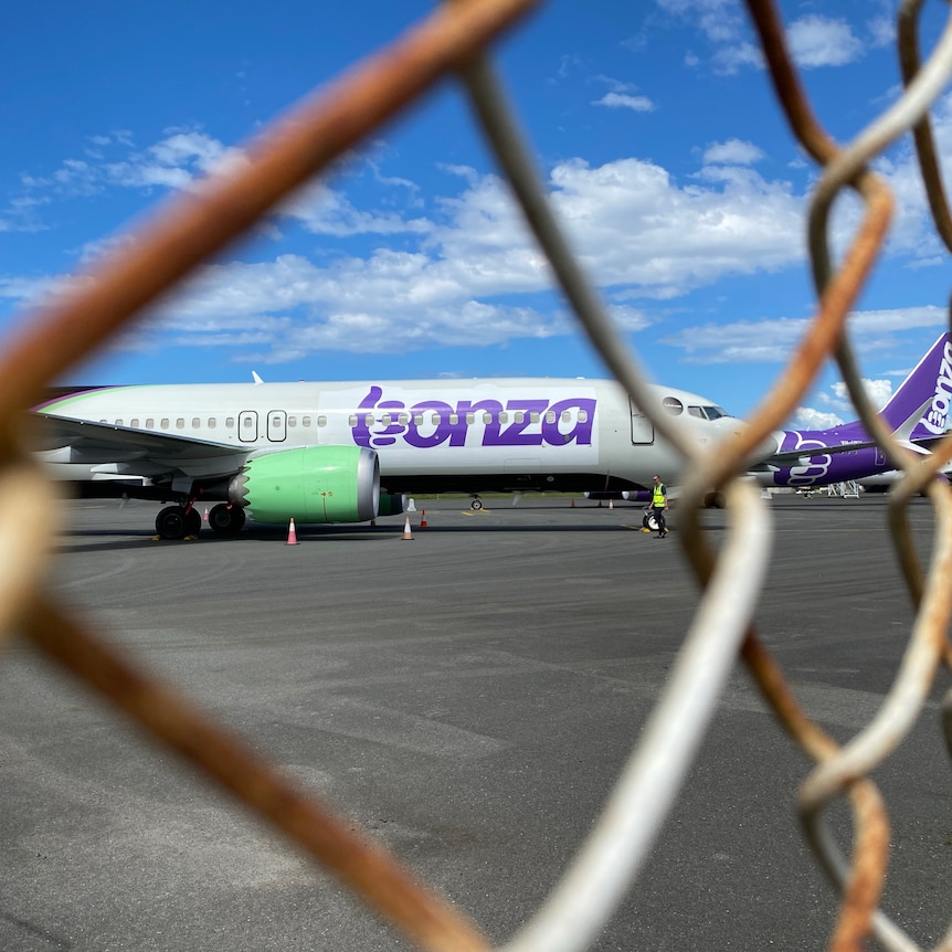 A Bonza plane sits on the tarmac behind a wire fence.