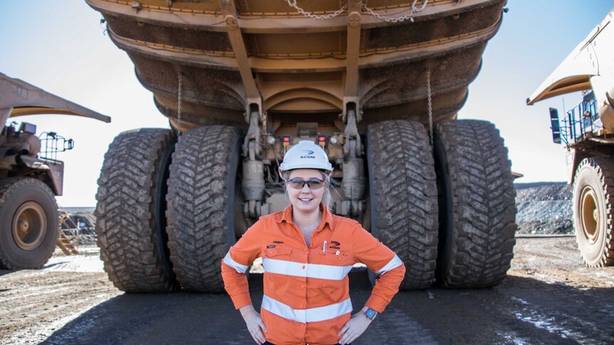 Woman standing next to tyre of big mining truck parked up
