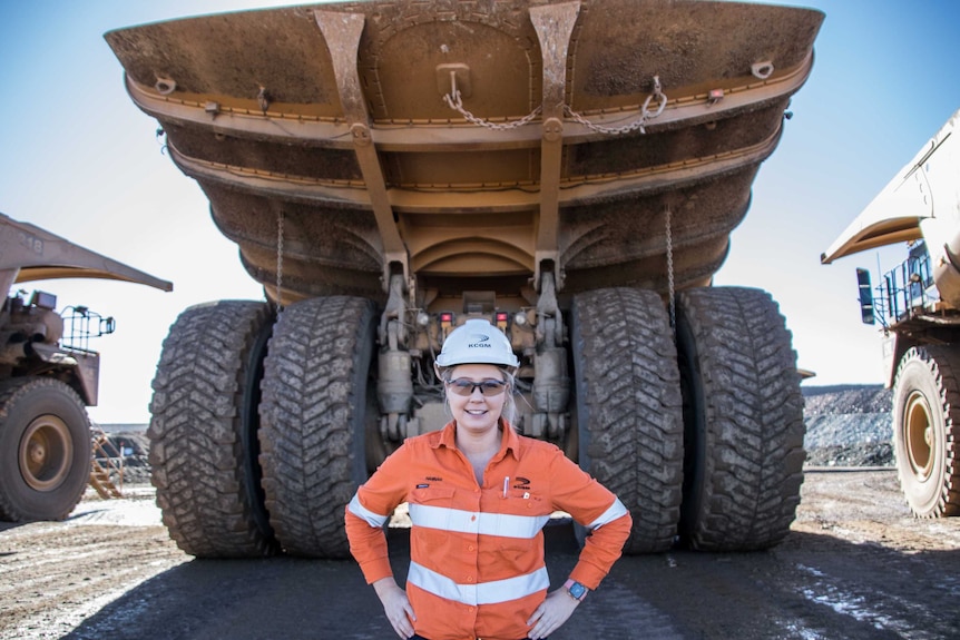 A woman standing next to tyre of big mining truck parked up
