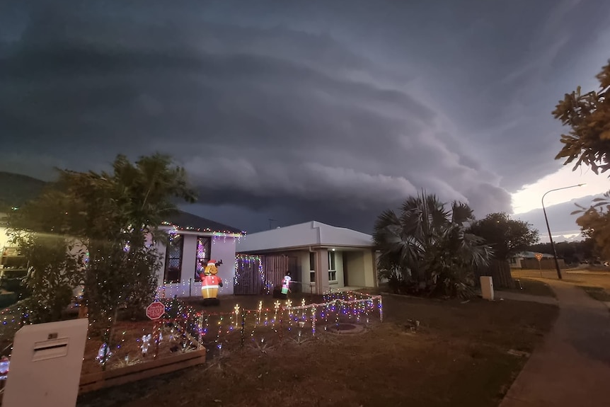 a house adorned with christmas lights looks dark underneath a big storm cloud
