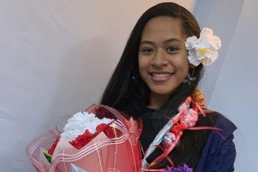 Samoan student Julie Eti smiles at the camera holding bunches of flowers. 