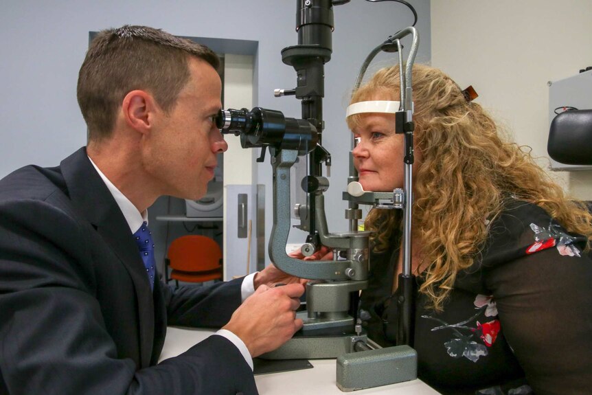 A doctor looking through equipment to examine a female patient's eye.