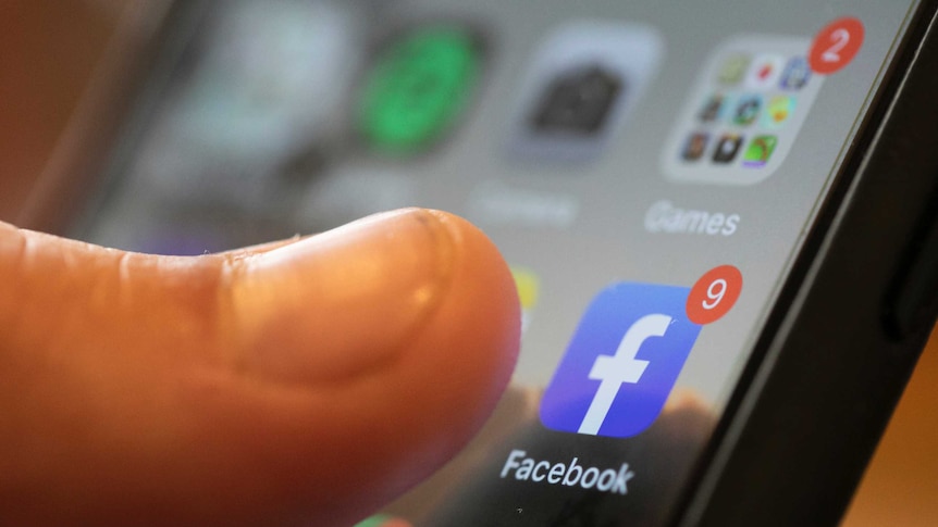 A finger touches the Facebook app on a smartphone