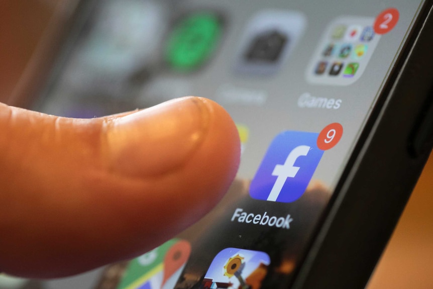 A finger touches the Facebook app on a smartphone.