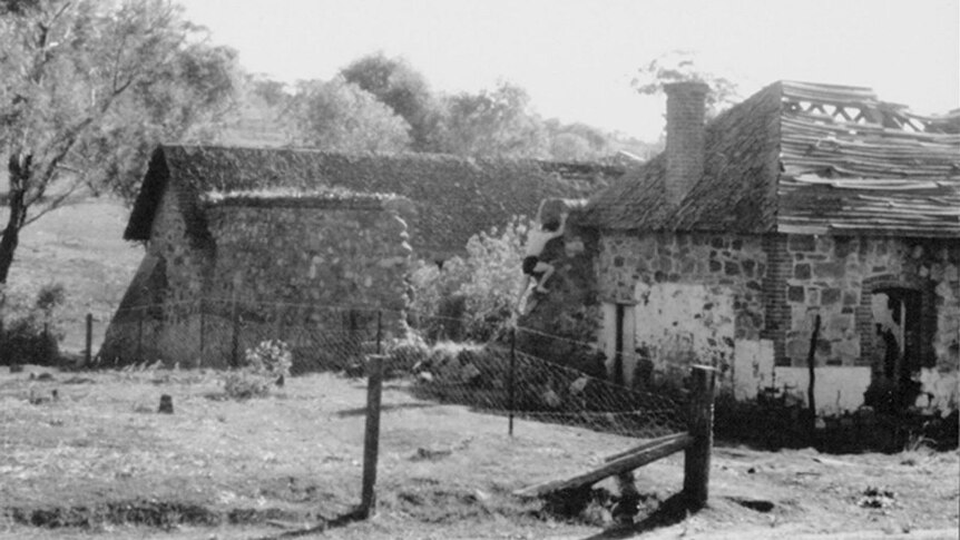 Black and white photo of a man climbing a small stone building's wall