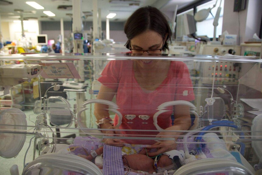 A woman smiling and feeding a premature baby in a hospital.