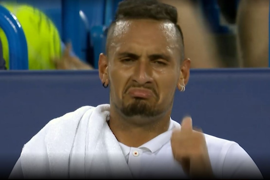 Nick Kyrgios gives a thumbs up and makes a sarcastic face while sitting on the bench.