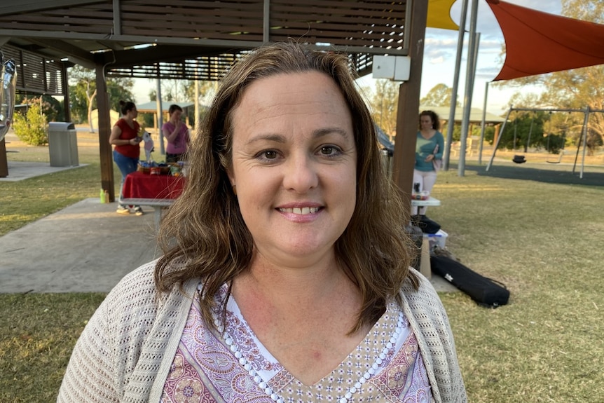 A woman with brown hair smiles. She is wearing a pink top.