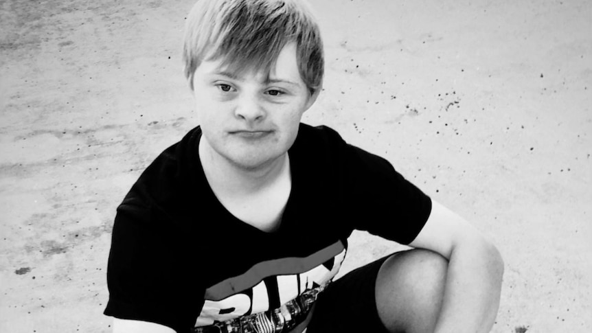 A white teenage boy with fair hair and Down syndrome sitting on the ground