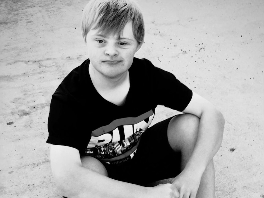 A white teenage boy with fair hair and Down syndrome sitting on the ground