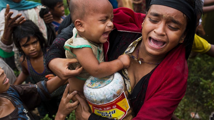 A woman holding a child looks distressed and upset and holds a food package at a refugee camp.