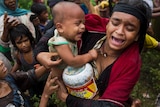 A woman holding a child looks distressed and upset and holds a food package at a refugee camp.