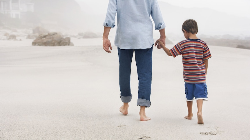 A father and son walk hand in hand on a beach