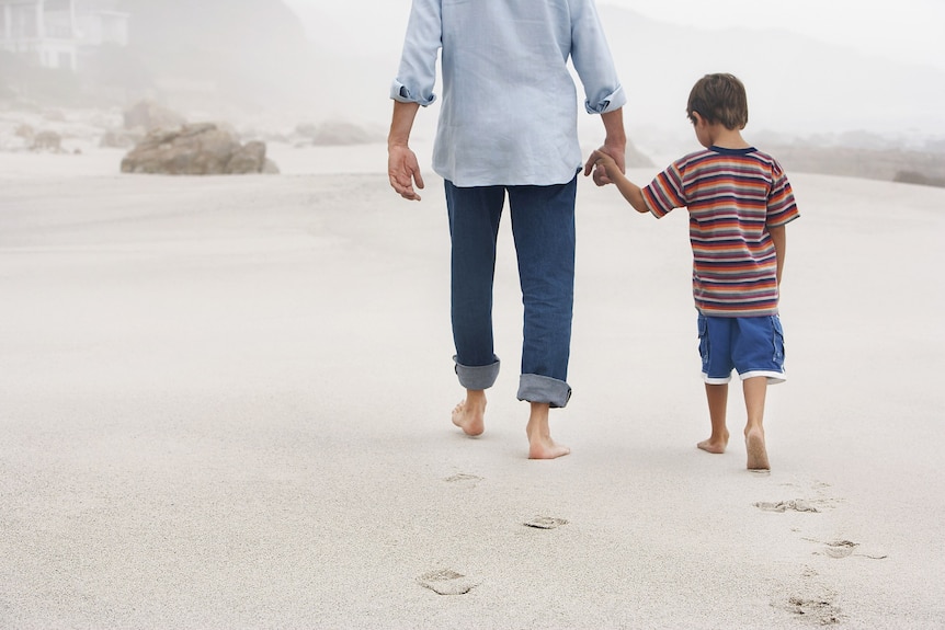 A father and son walk hand in hand on a beach
