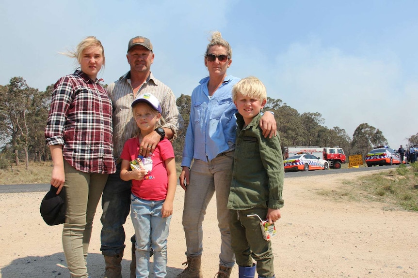 A family of five standing in front of emergency vehicles.