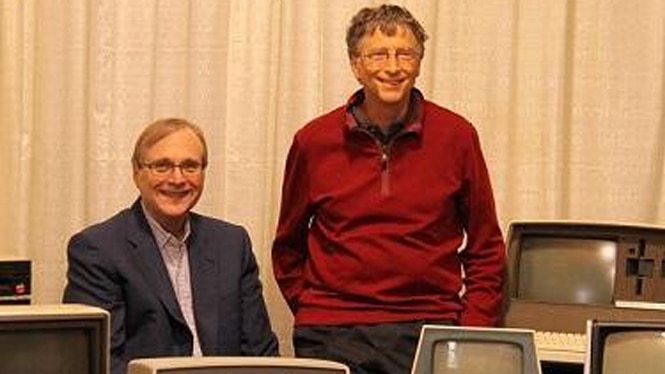 Two men stand behind a range of anique computers