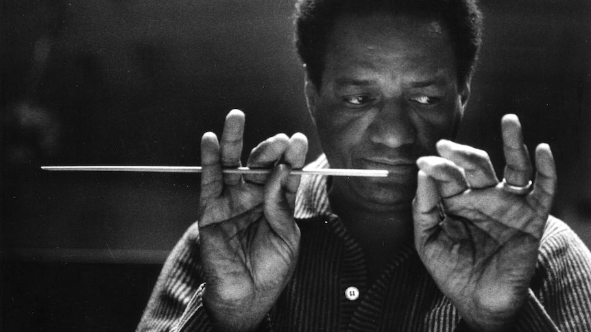 Close up portrait of Afro-American conductor with hands raised, palms ooutward, with baton