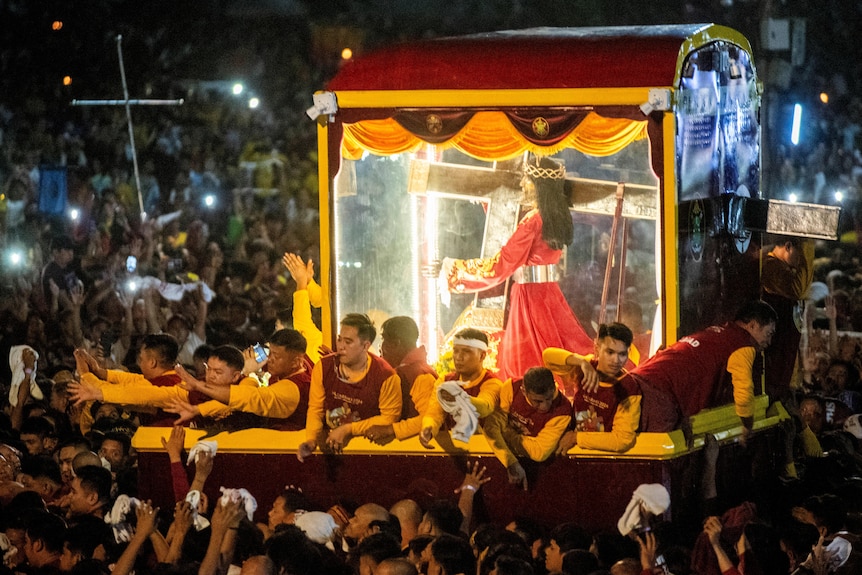 the statue of the Black Nazarene seen in a glass carriage surrounded by crowds.