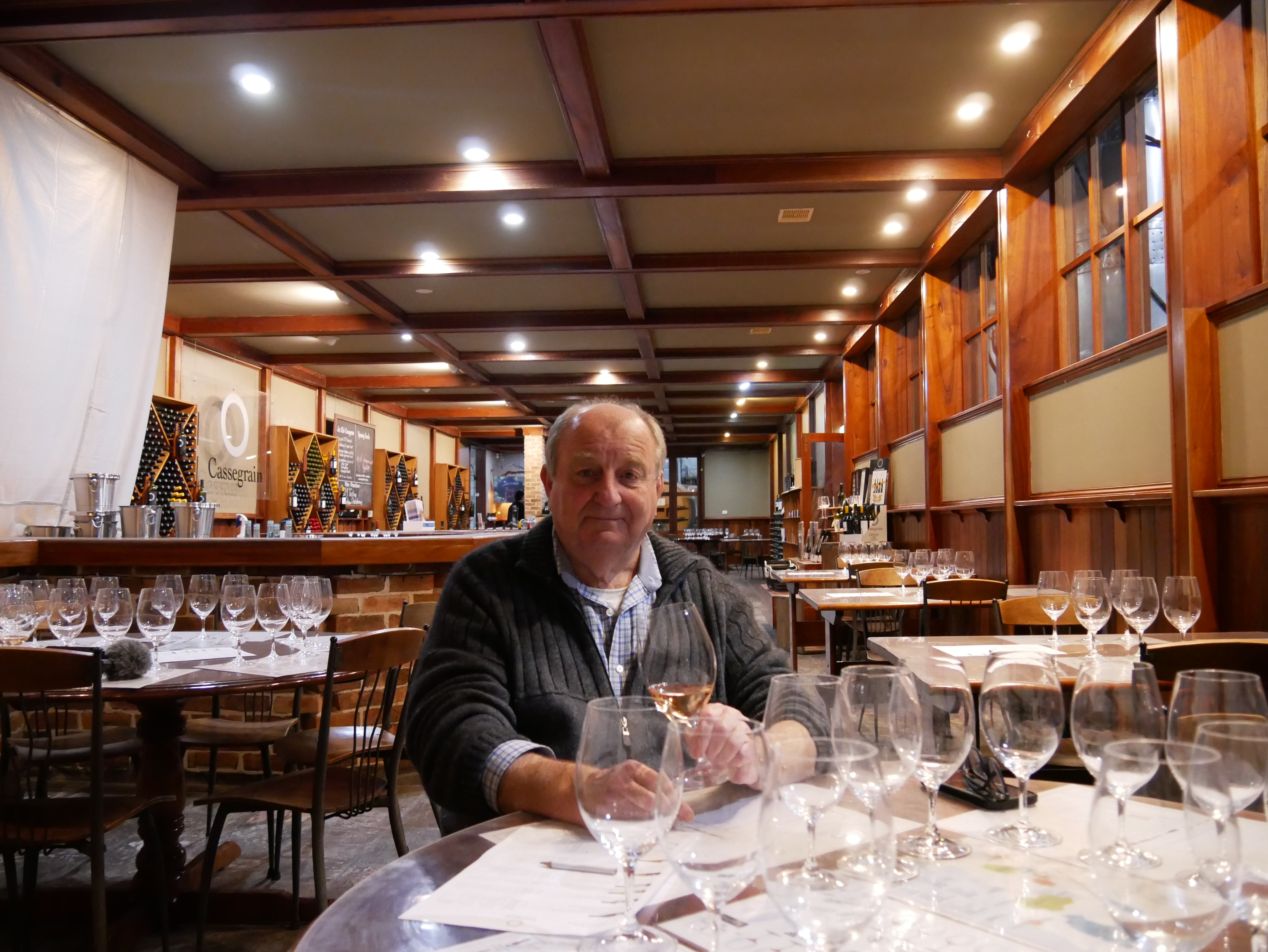 An older man sitting in his winery with a glass of wine in hand.