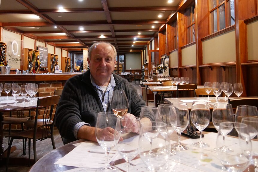 An older man sitting in his winery with a glass of wine in hand.