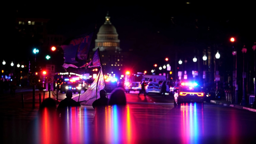 Supporters of President Donald Trump hold flags as lights from police vehicles illuminate Pennsylvania Avenue in Washington.