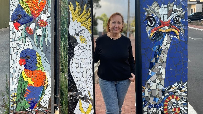 colourful mosaic art on pole in the form of birds and a smiling woman in a black top