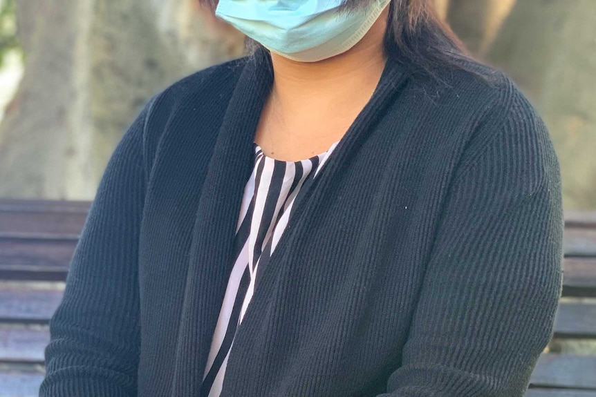 A woman whose face is not visible sits on a park bench.