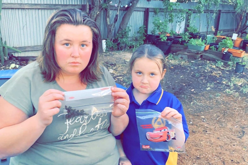 Sad mother and daughter sitting in garden holding sandwich bags filled with dead bees.