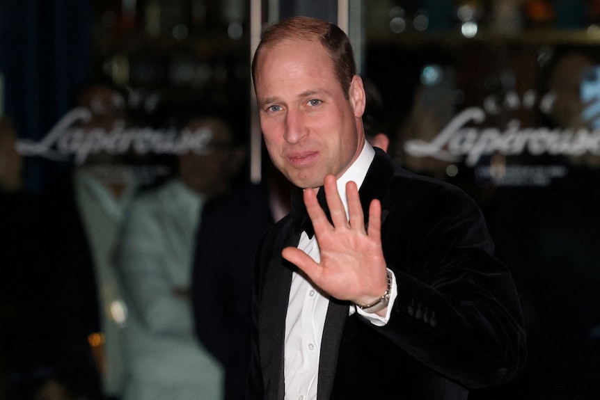 Prince William in a tuxedo waves at the media 