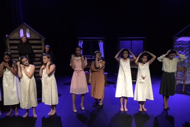 The cast, dressed in nightgowns stand in a line onstage