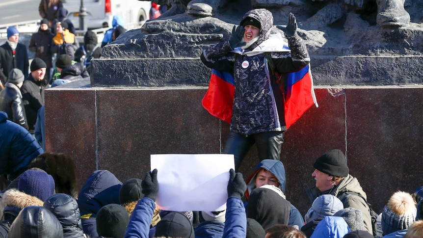 A demonstrator with a Russian national flag wrapped in his shoulders shouts slogans during a rally in Russia