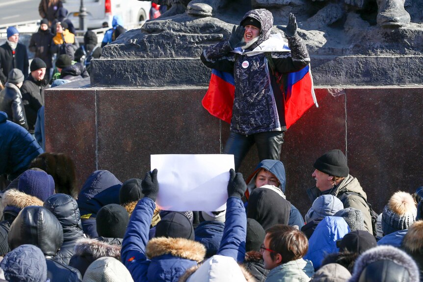 A demonstrator with a Russian national flag wrapped in his shoulders shouts slogans during a rally in Russia