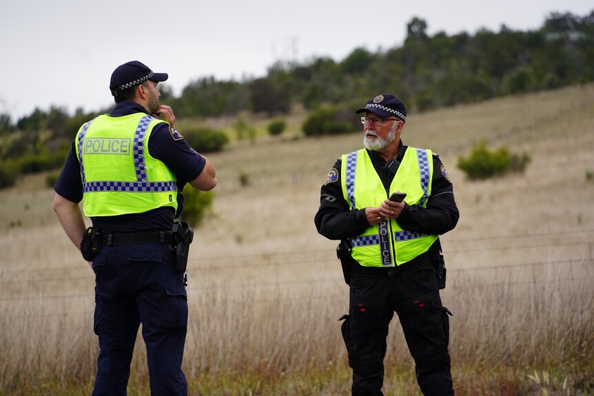Two police officers talk to each other on the side of a road