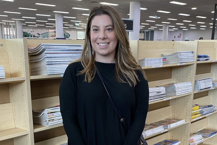 A young woman stands in front of bookshelves and smiles into the camera.