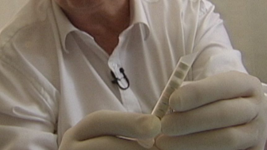 A person, wearing surgical gloves, holds an injectable device