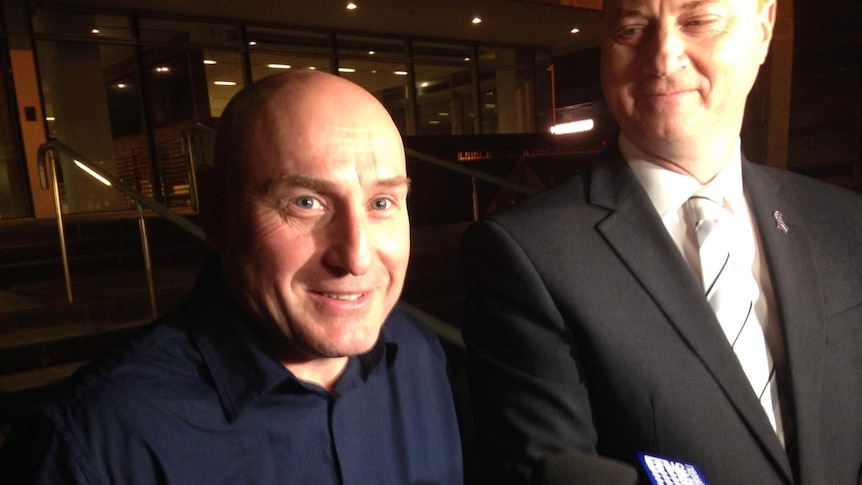 A smiling WA Police Senior Constable Andrew Swift stands by WA Police Union president George Tilbury outside court at night.