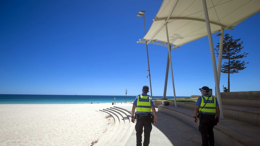 Police wear face masks while patrolling Scarborough Beach in Perth. On a beautiful, blue-sky day, the beach is mostly empty.