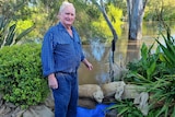  a man stands next to floodwater and sandbags