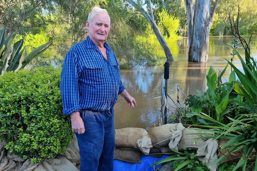  a man stands next to floodwater and sandbags