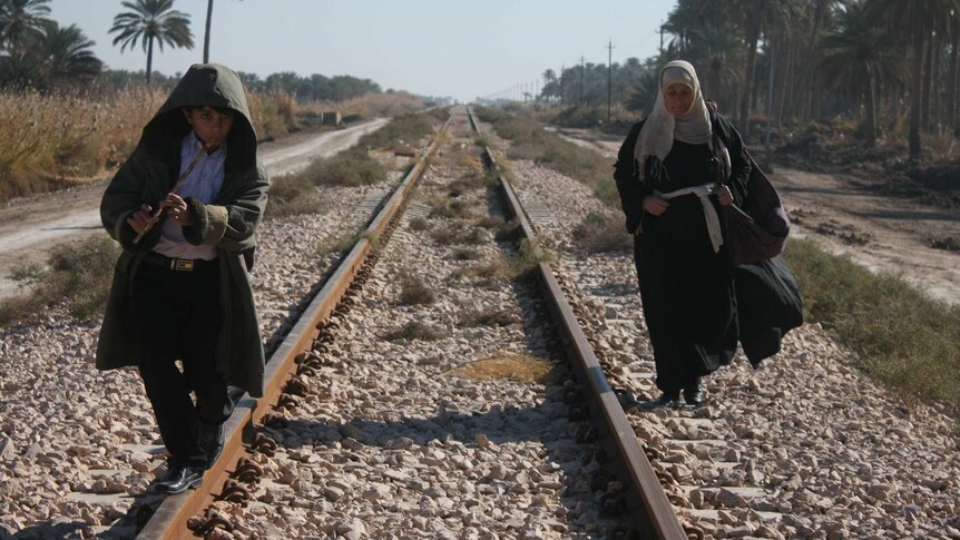 A young boy and his grandmother walk along train tracks in Iraq.