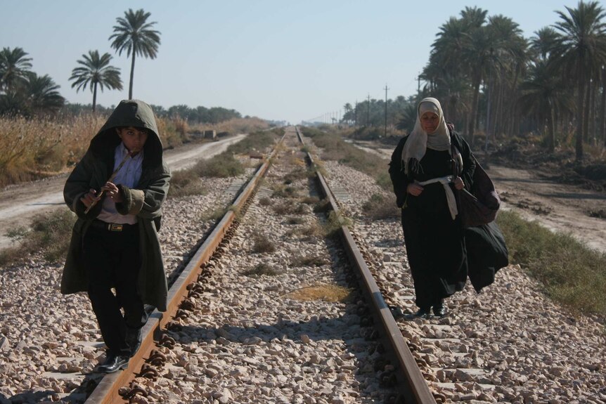 A young boy and his grandmother walk along train tracks in Iraq.