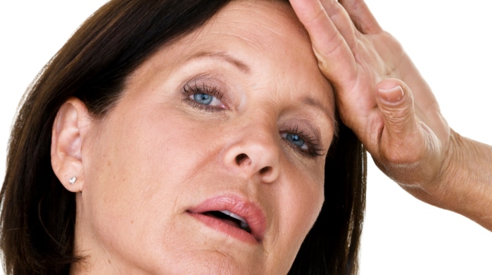 A picture of a middle aged woman with her hand to her forehead, possibly feeling hot